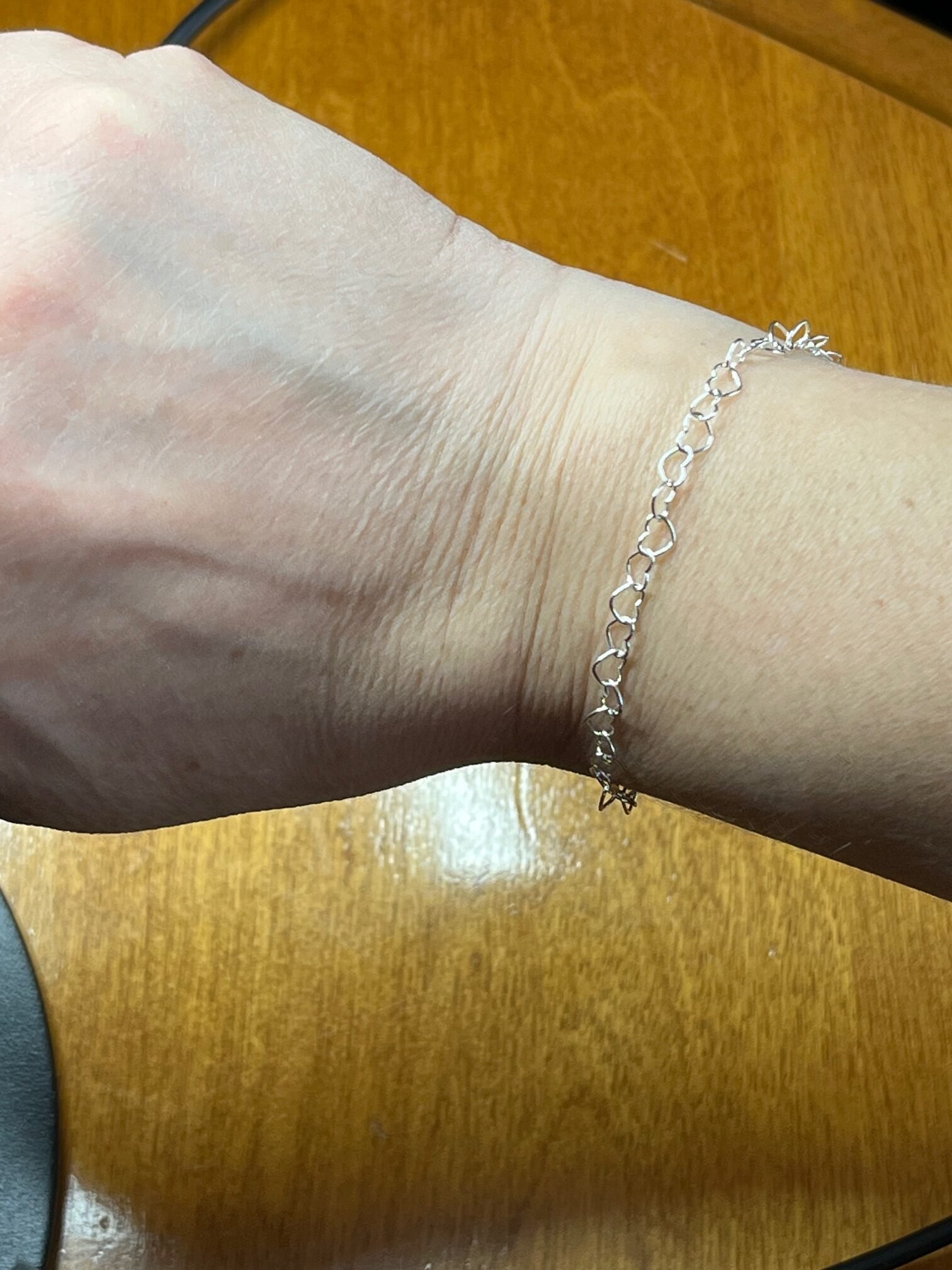 A silver heart-link bracelet fitted around a wrist