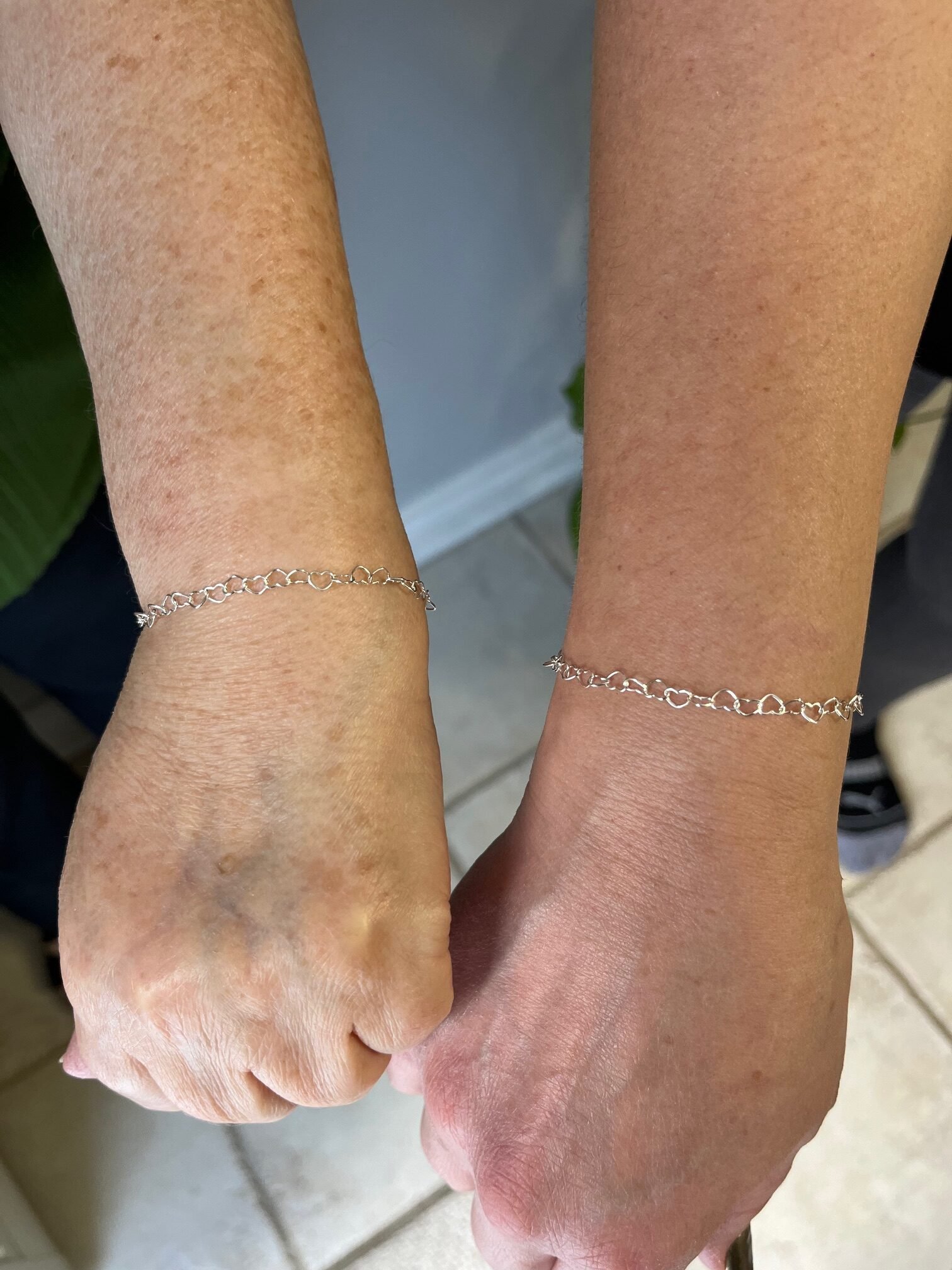 Two wrists displaying delicate silver heart-link bracelets