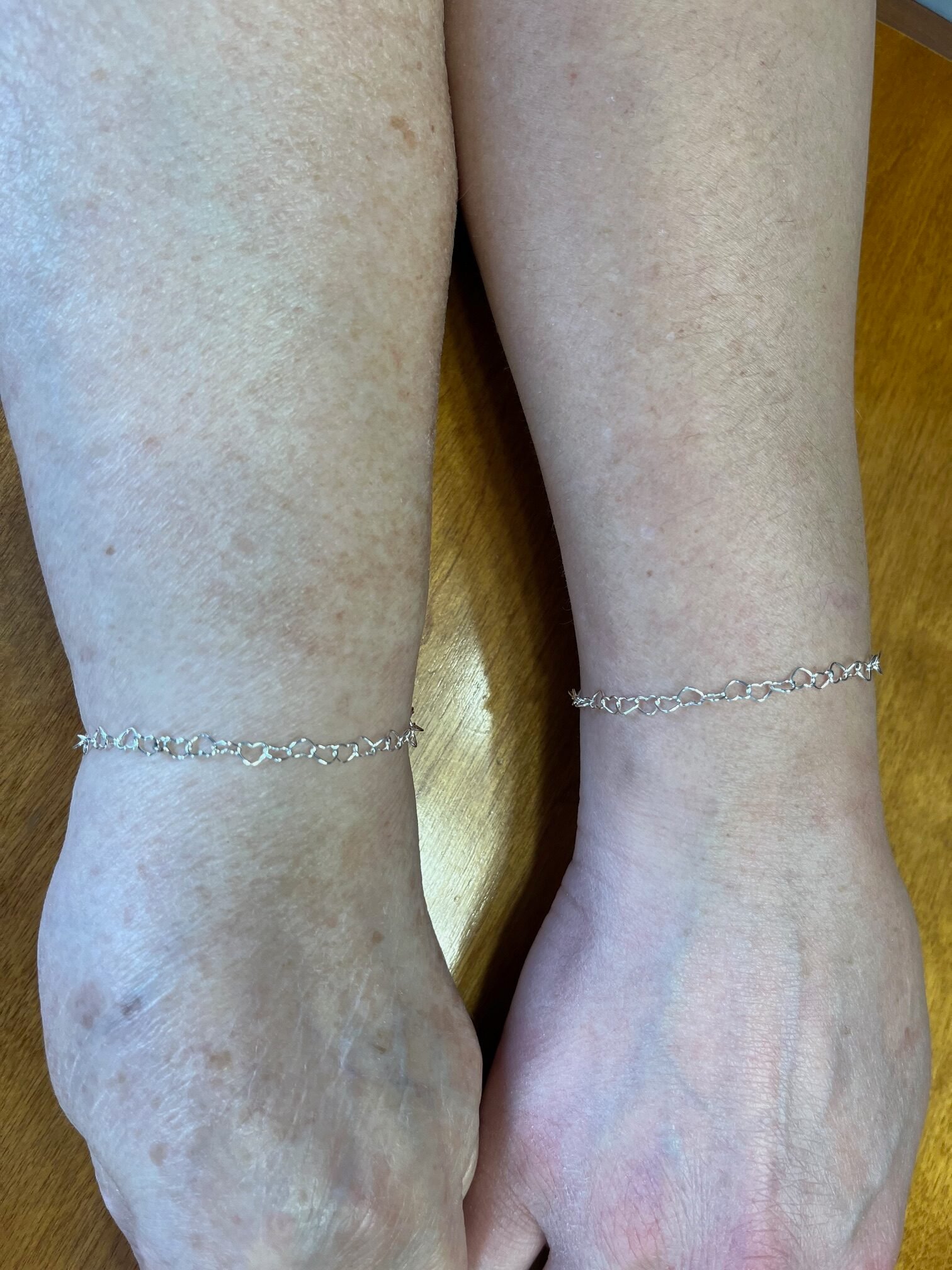 Close view of matching silver heart-link bracelets on two wrists
