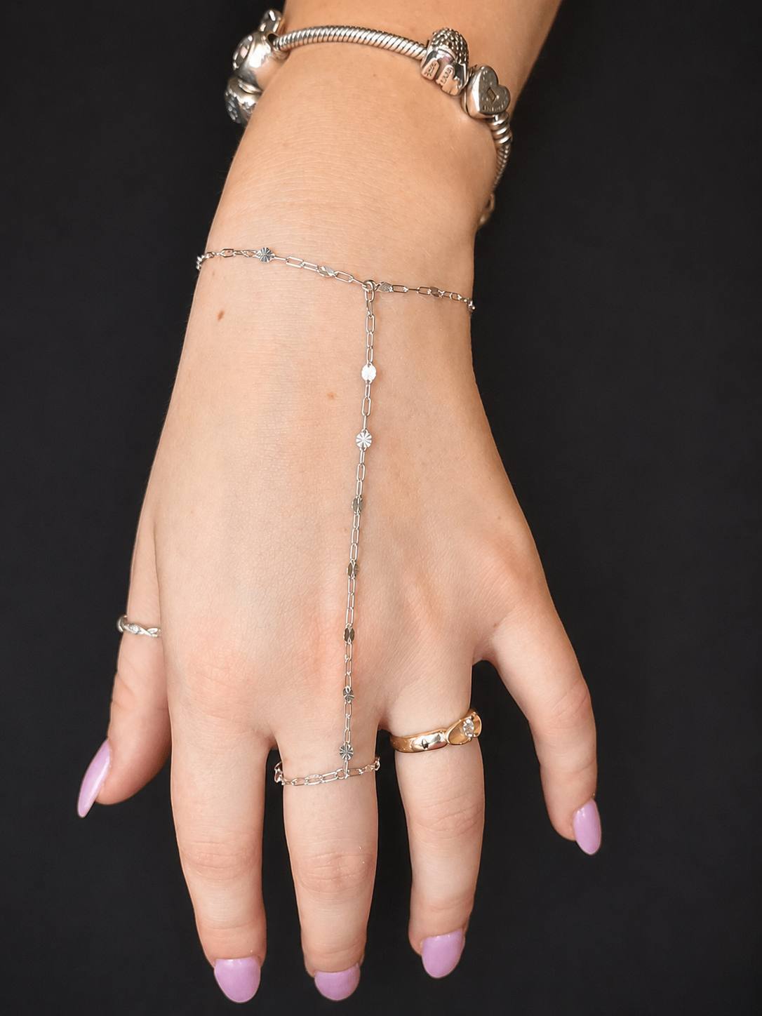 Silver hand chain, fitted to the hand against a dark background